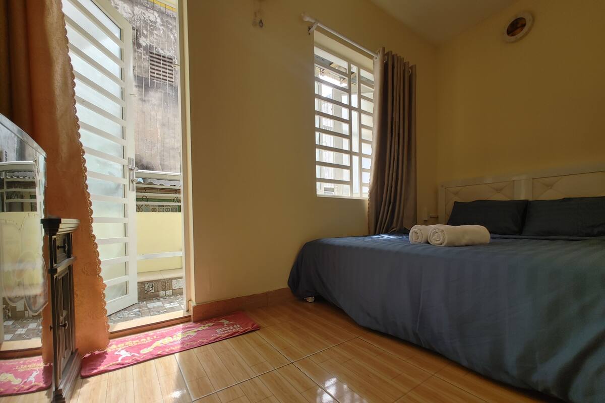 A hotel room with a bed, a window with curtains, a radiator, and a wooden floor.