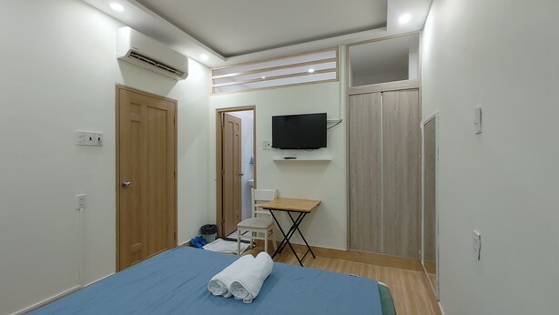 A bedroom with a bed, a TV mounted on the wall, a desk with a chair, and a wardrobe. - D Home (Ho Chi Minh City)