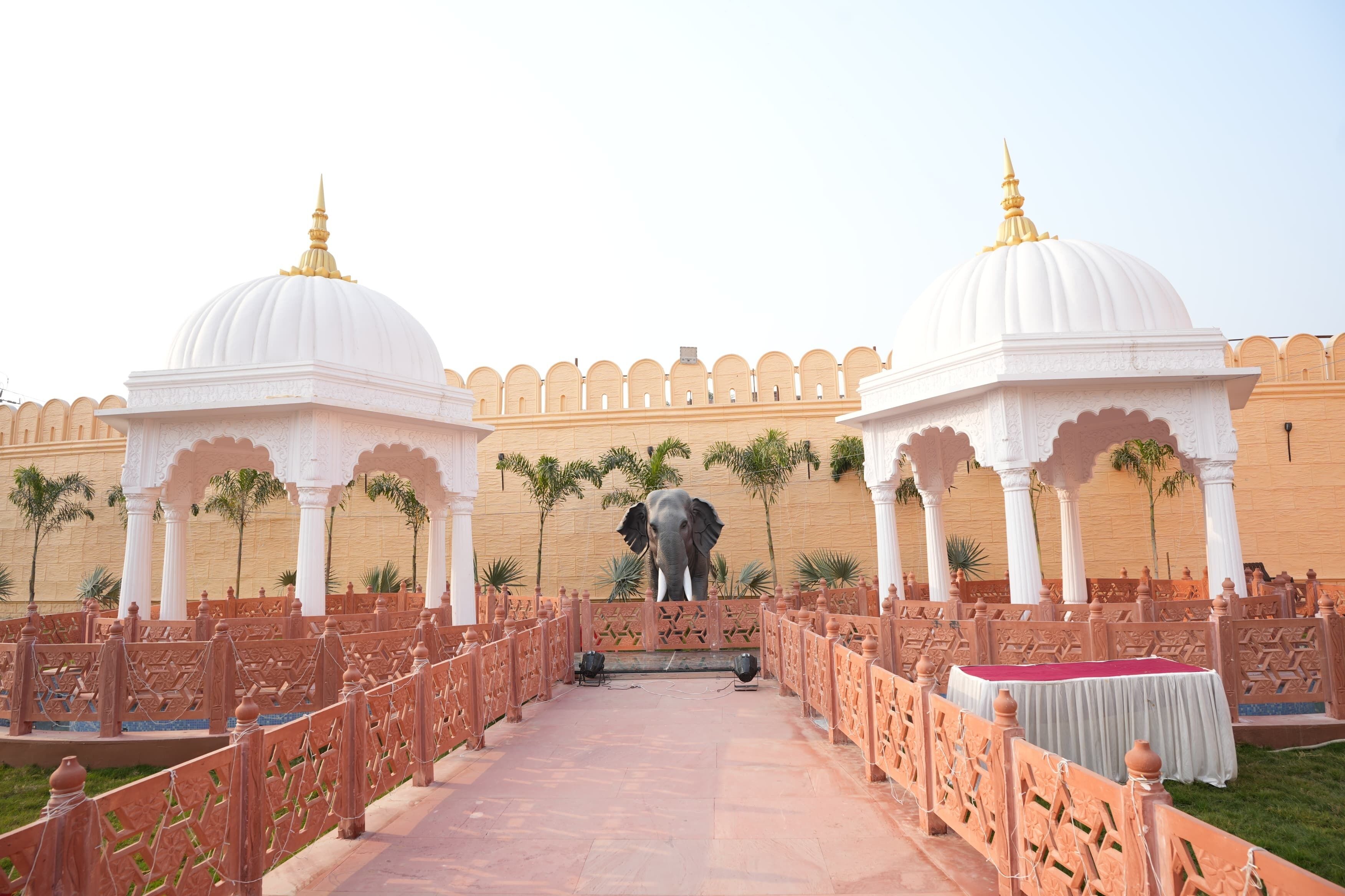 A corridor with white domed structures and an elephant statue, leading to a seating area with a table.