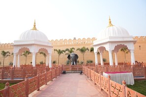 A corridor with white domed structures and an elephant statue, leading to a seating area with a table. - Hotel Banaras kila (Pindra)