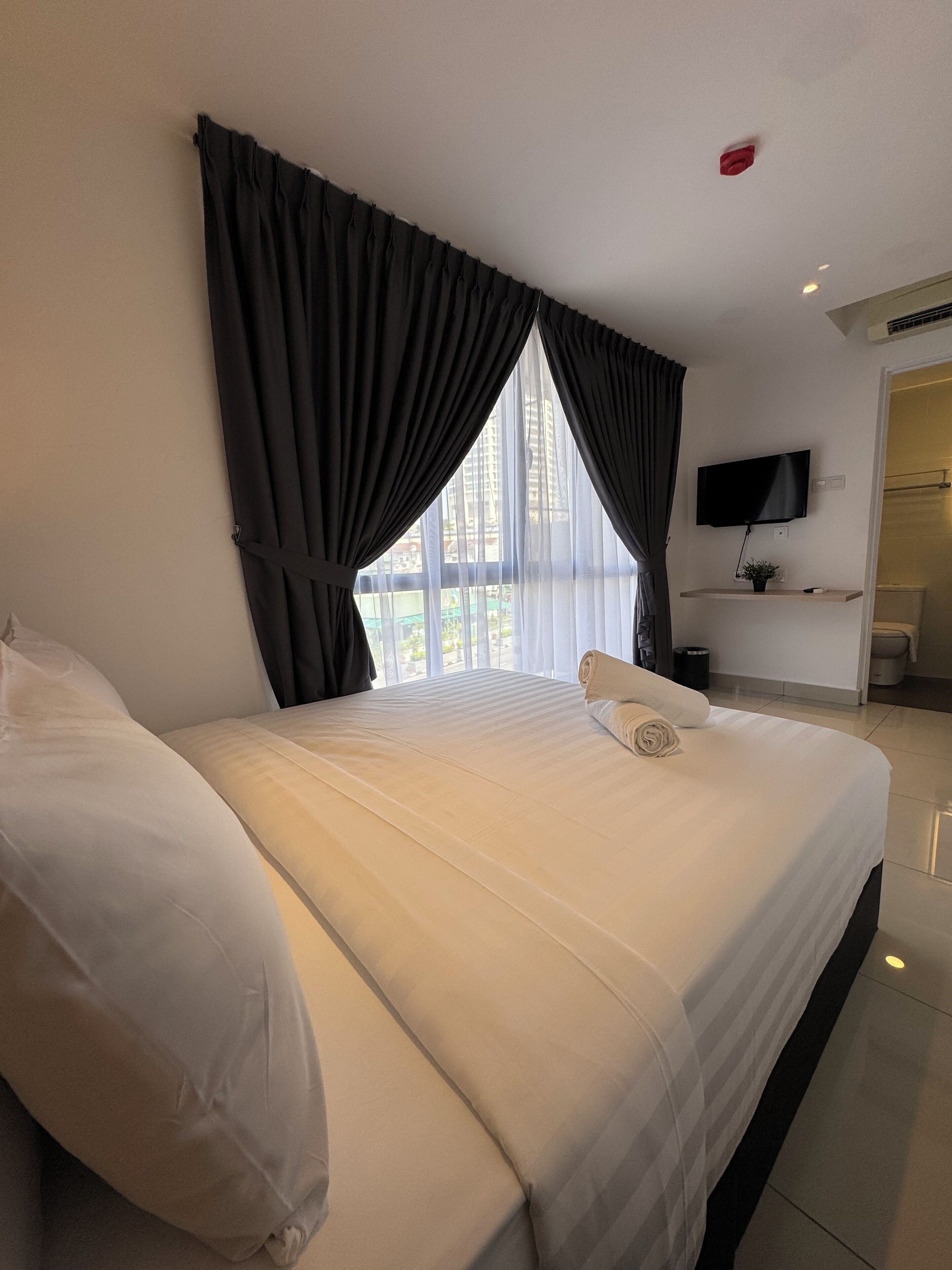 A hotel room with a large bed, a flat-screen TV mounted on the wall, and a window with curtains.