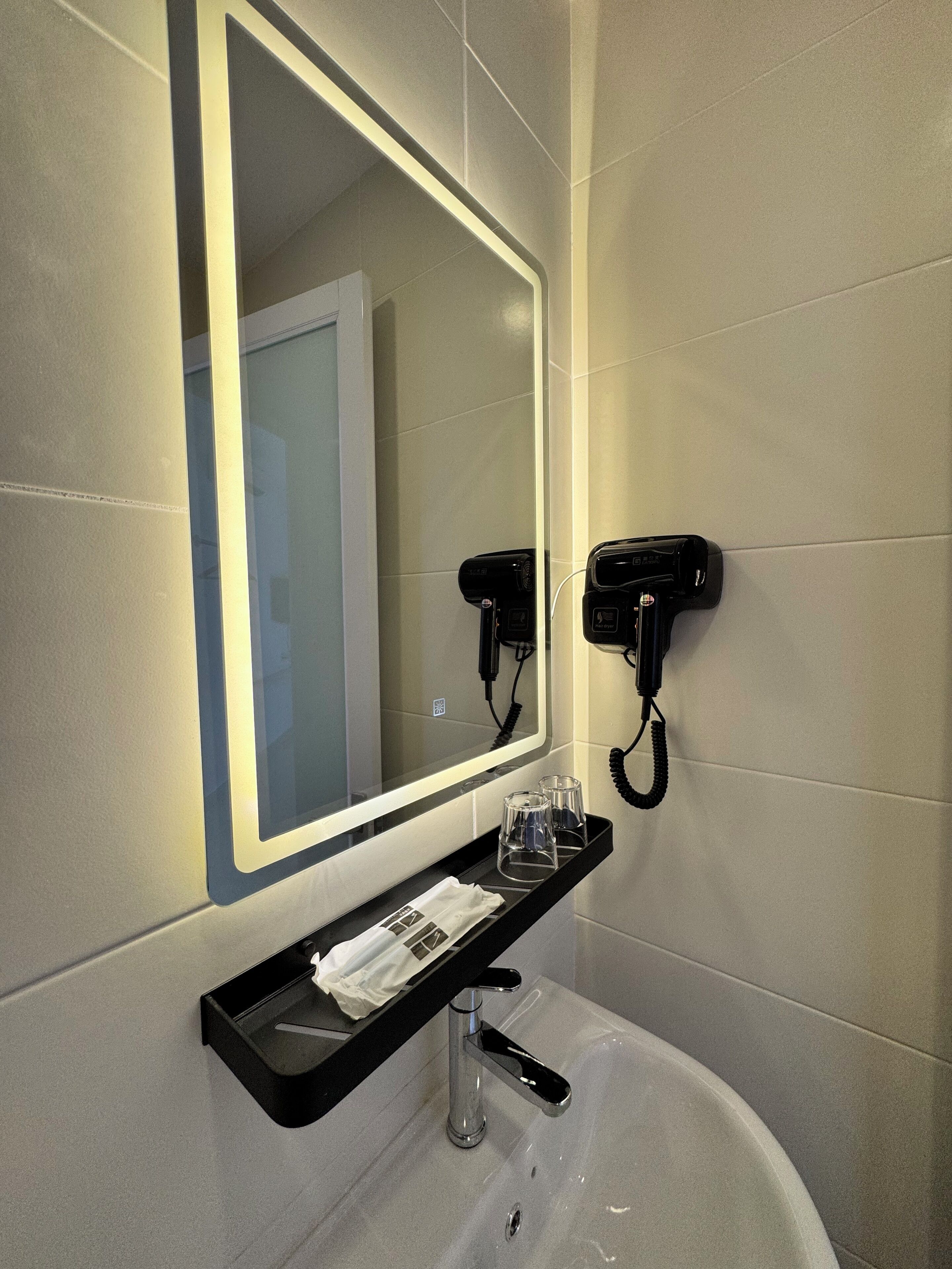 A bathroom with a large mirror, a black telephone, and a tray with glasses and a tissue.