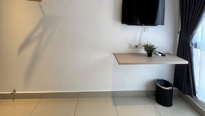 Una sala moderna con un televisor de pantalla plana montado en un estante de madera, un equipo de aire acondicionado en el techo, un cubo de basura negro y una ventana con cortinas.