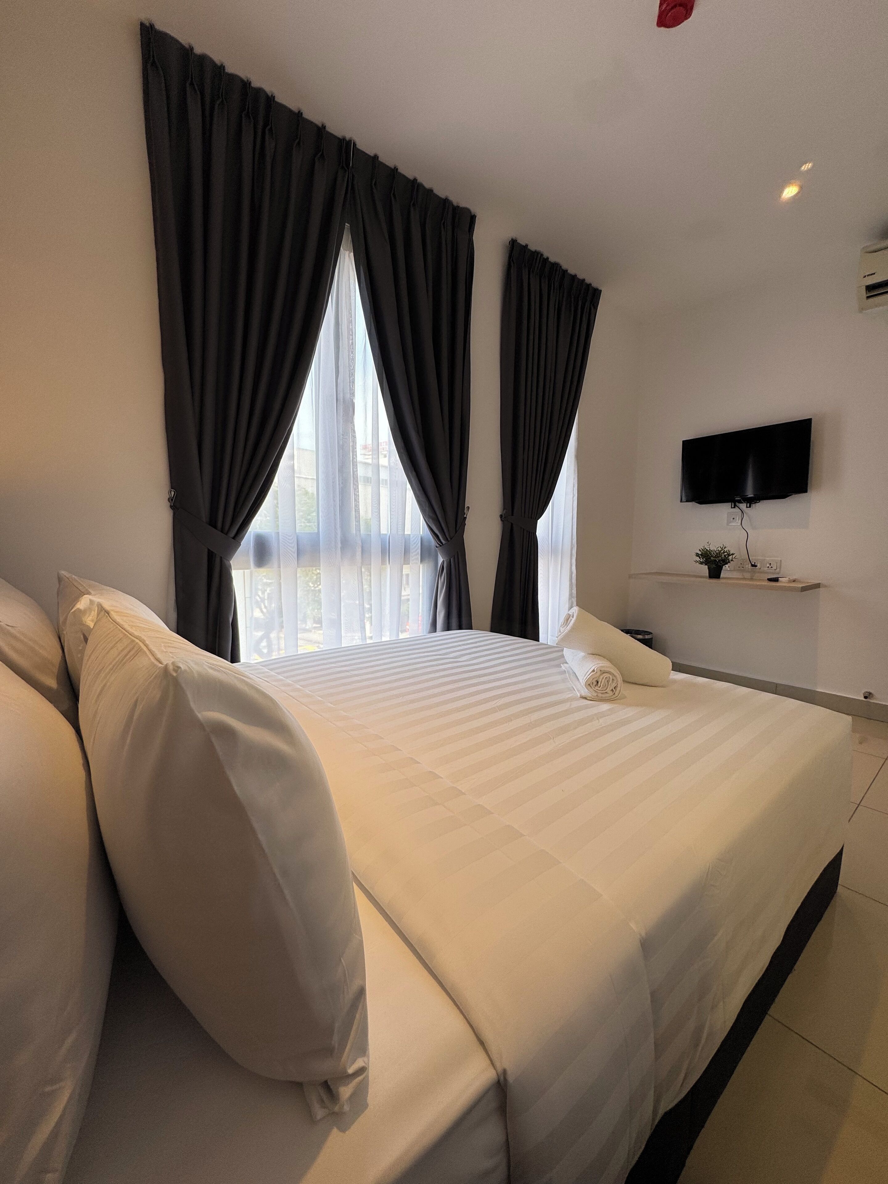 Une chambre d’hôtel avec un grand lit, un téléviseur à écran plat fixé au mur et une fenêtre avec des rideaux.