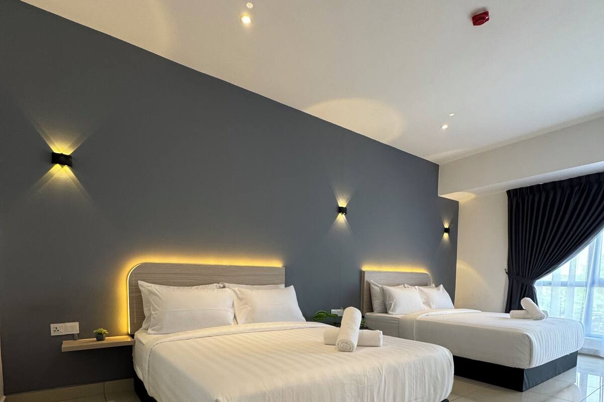 A modern hotel room with two beds, a large window with curtains, and wall-mounted lighting.
