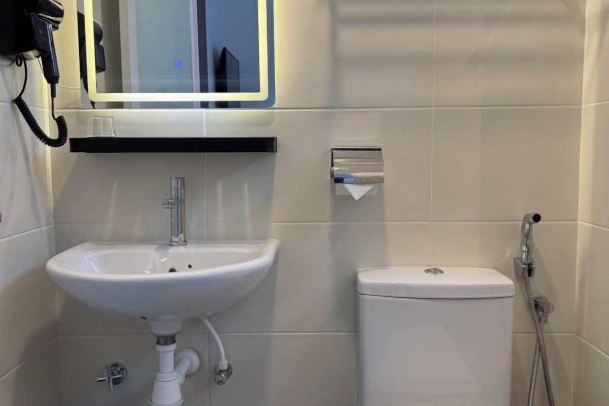 Egy fürdőszoba, melyben fehér mosdókagyló, WC és egy tükör található, a falra pedig egy telefon van szerelve.