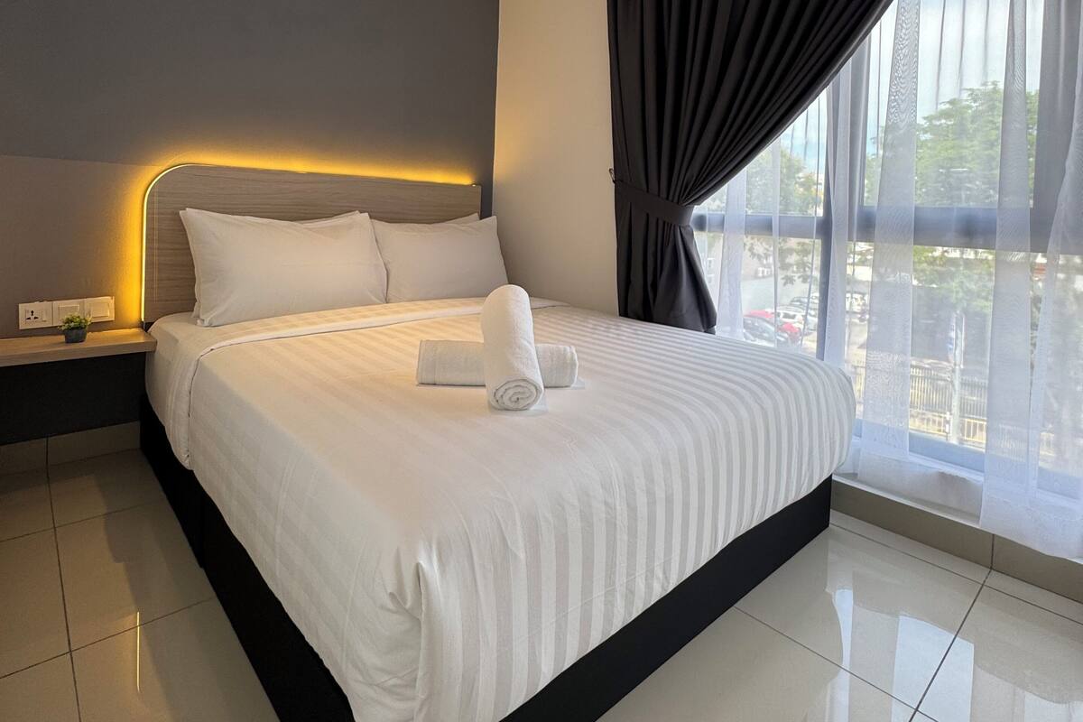 A modern hotel room with a large bed, a bedside table, a nightstand, and a view of the outdoors.