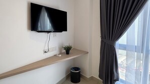 Una habitación moderna y minimalista con un televisor de pantalla plana montado en la pared, un pequeño estante con una planta y un cesto de basura negro.