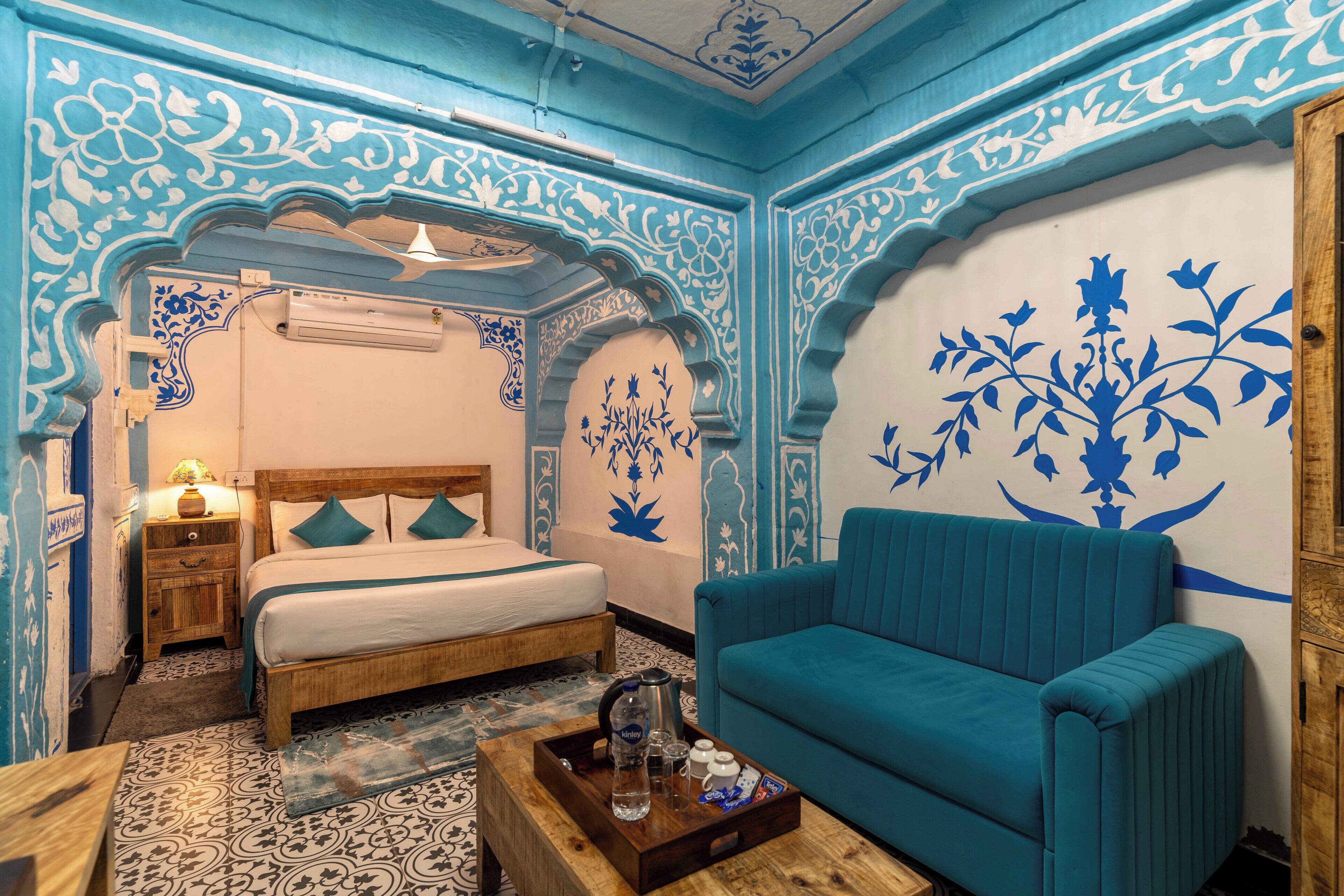 Una habitación con una cama, un sofá, una mesa de centro de madera con una bandeja y una pared decorada con motivos florales azules.
