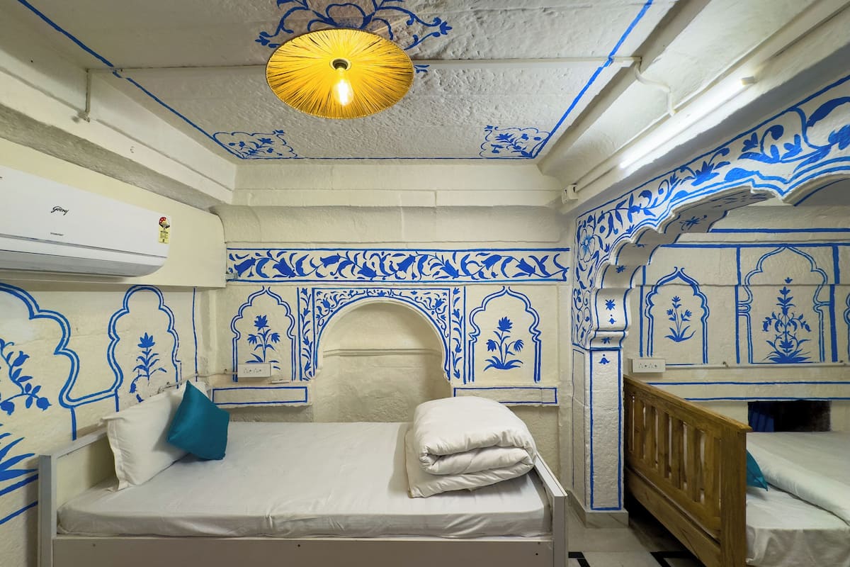 Ein Zimmer mit einem Bett, einer hölzernen Bank und blauen dekorativen Mustern an Wänden und Decke.