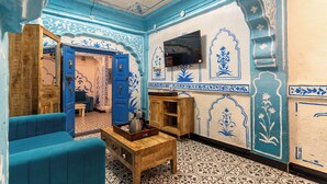 Ein Zimmer mit Wänden in blau-weißem Muster, einem Holzschrank, einer blauen Couch und einem Holztisch mit Tablett.