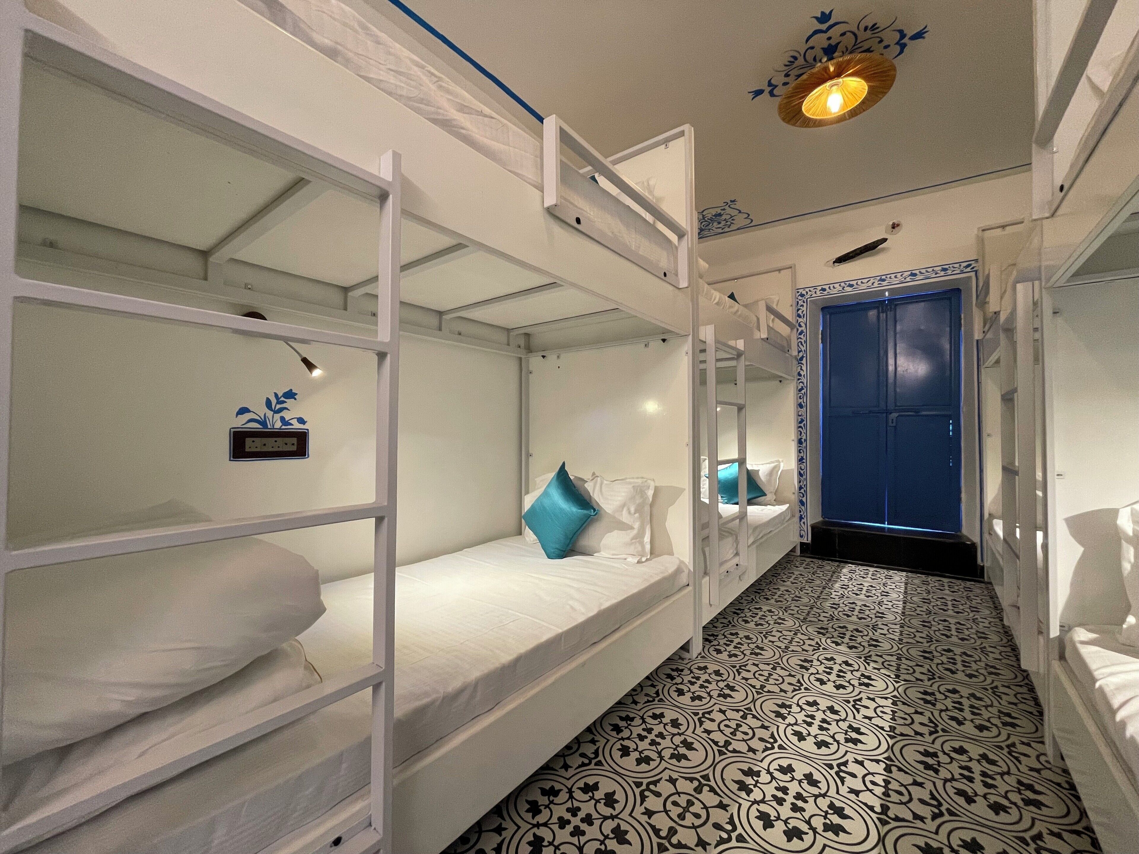 Ein Schlafraum mit Etagenbetten, einem gemusterten Boden, einer blauen Tür und einer Wandleuchte.