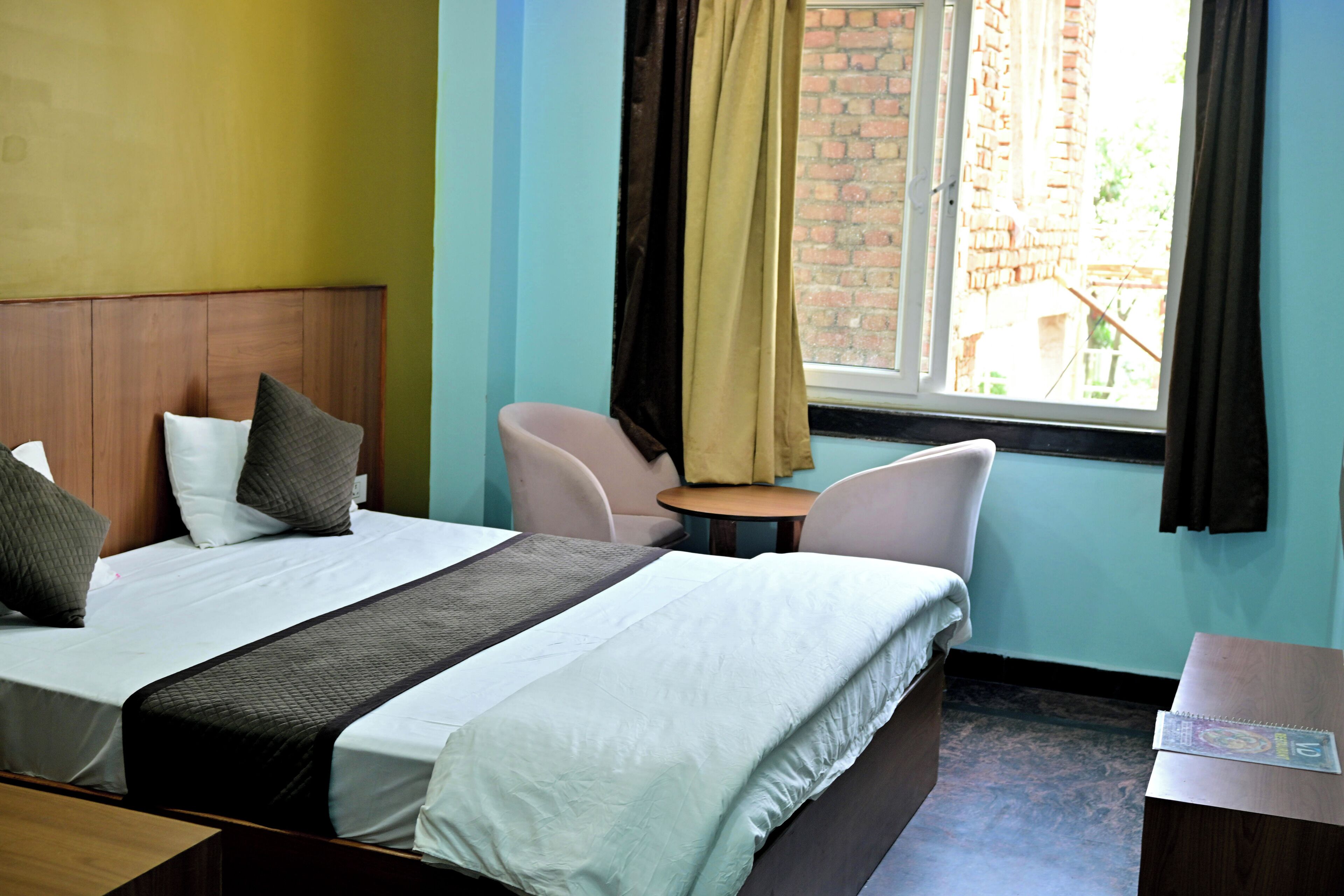 Una habitación de hotel con una cama, dos sillas, una mesita y una ventana con cortinas.