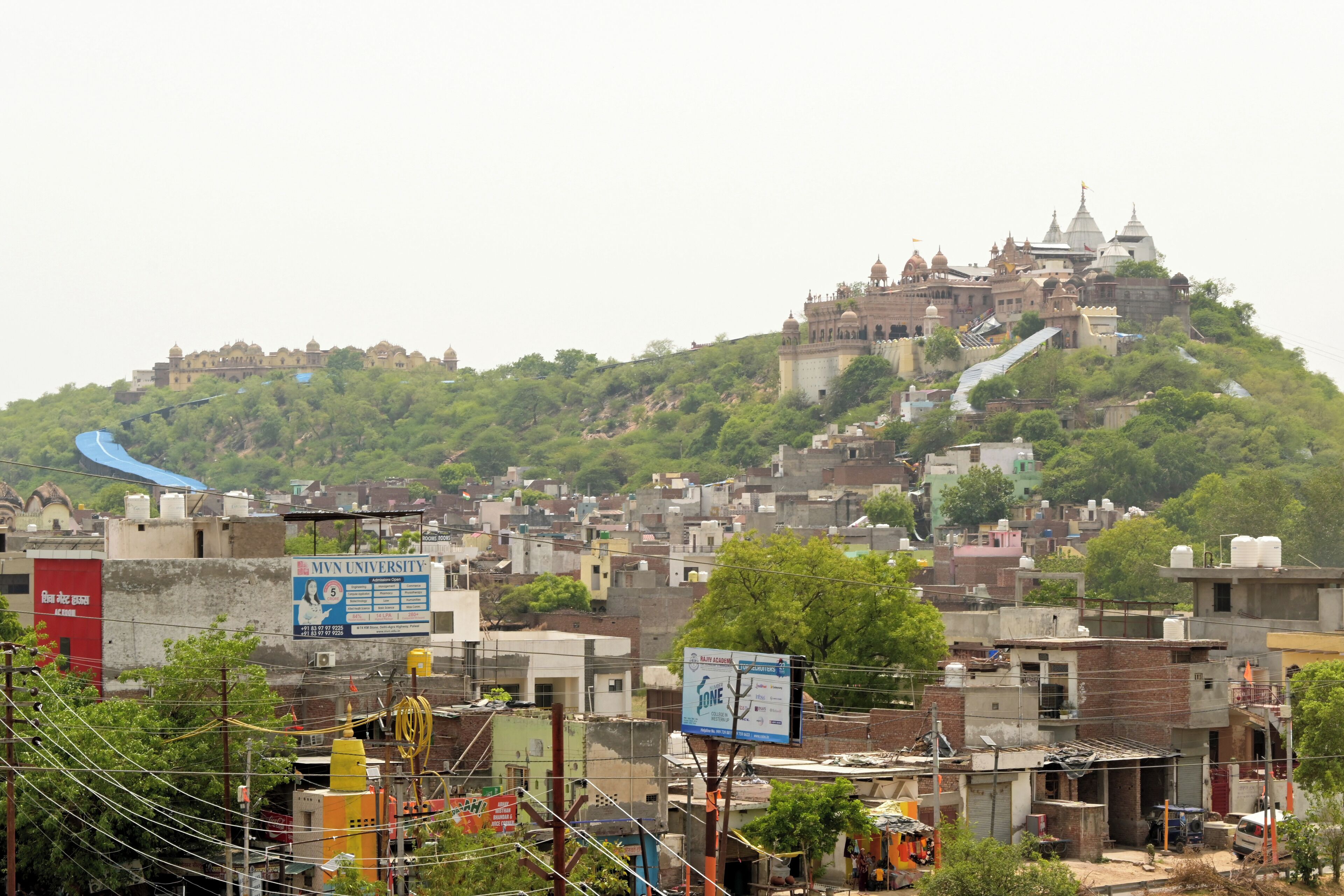 A hilltop temple complex with multiple domes and spires, surrounded by dense urban buildings and greenery.