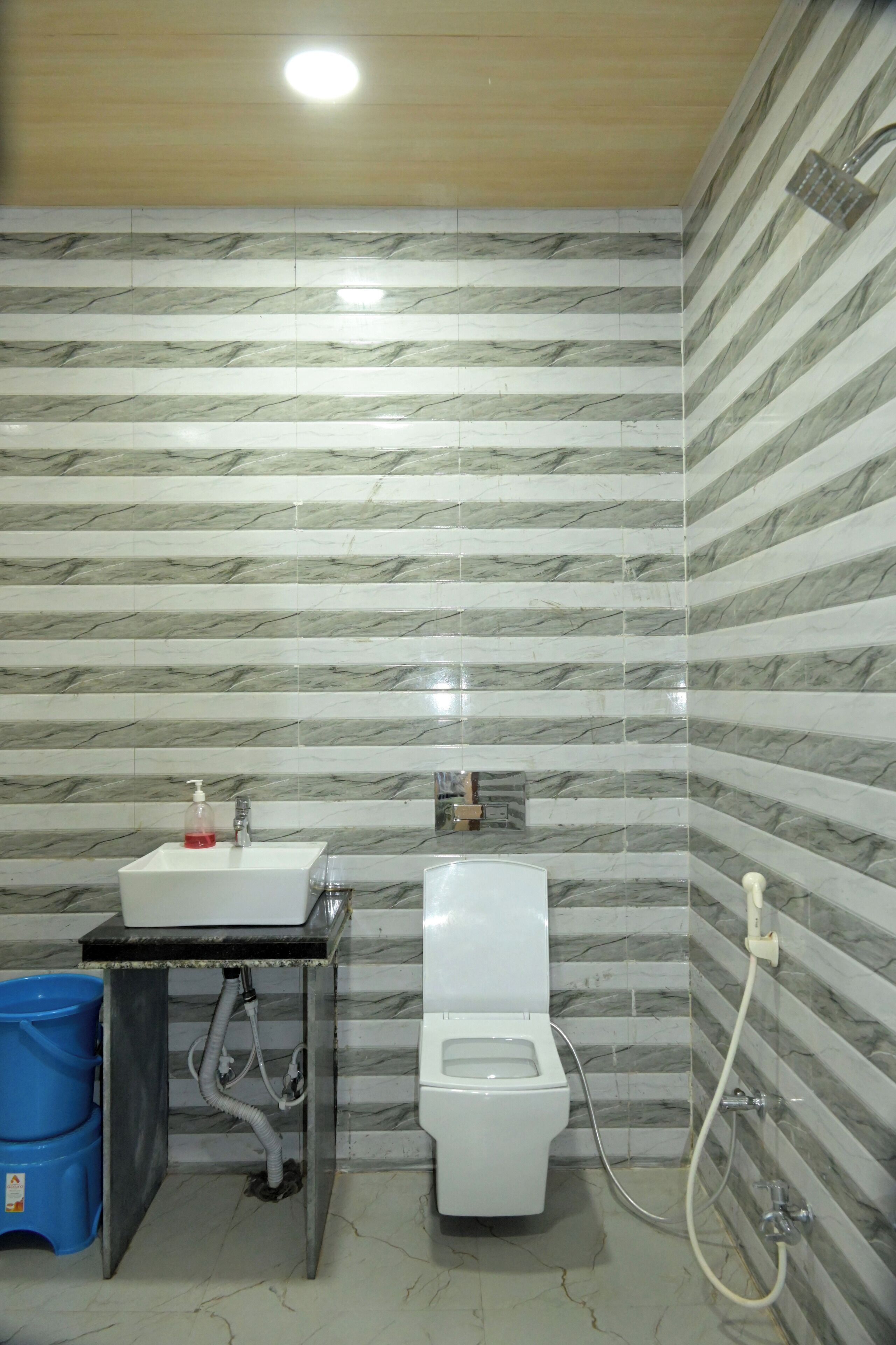 A bathroom with a marble-patterned wall, a sink with a soap dispenser, a toilet, and a shower.