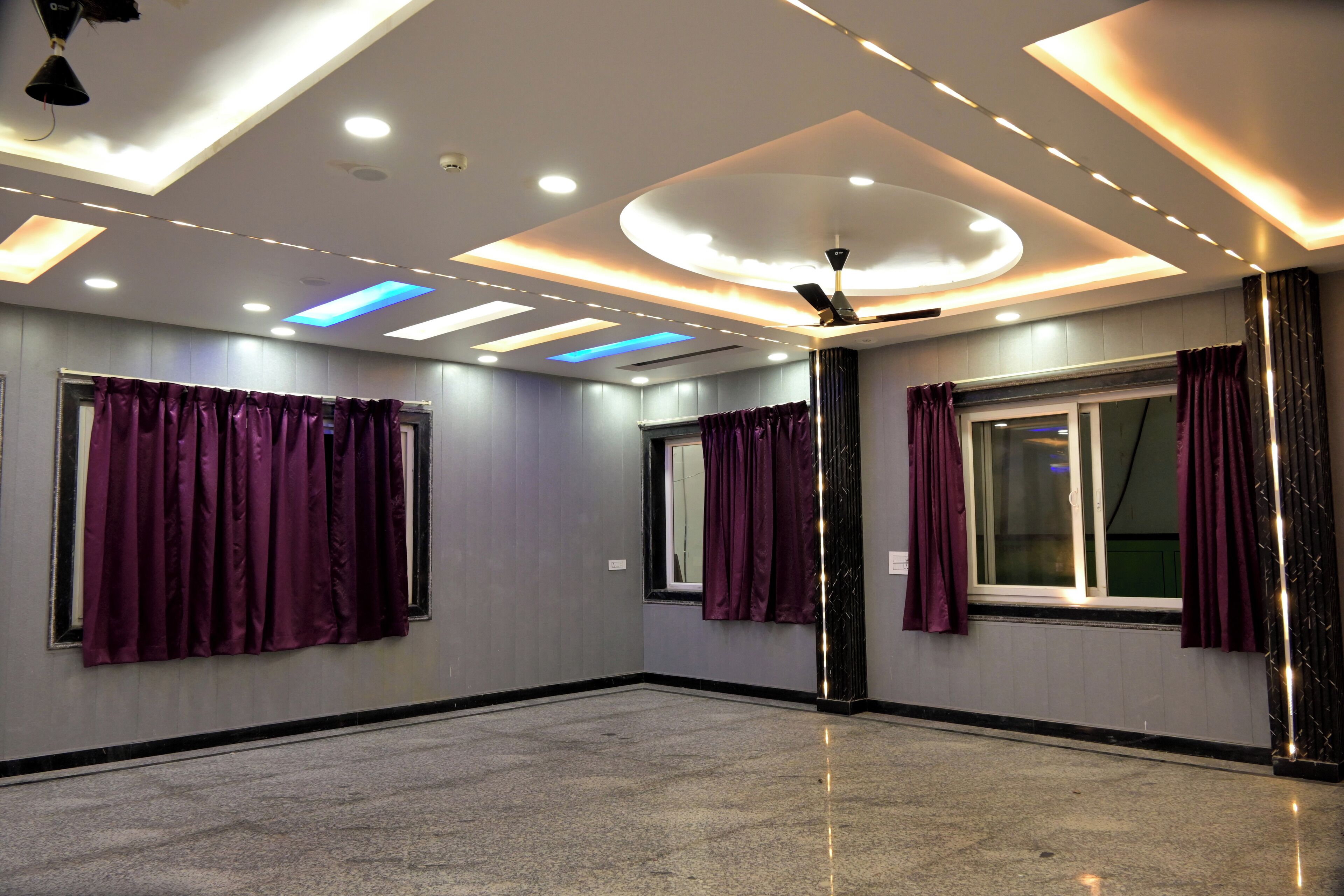A modern hotel room with a large window, purple curtains, a ceiling fan, and recessed lighting.
