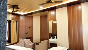 Habitación de hotel con dos camas, zona de estar con una silla y una mesa, ventilador de techo y paneles de madera.