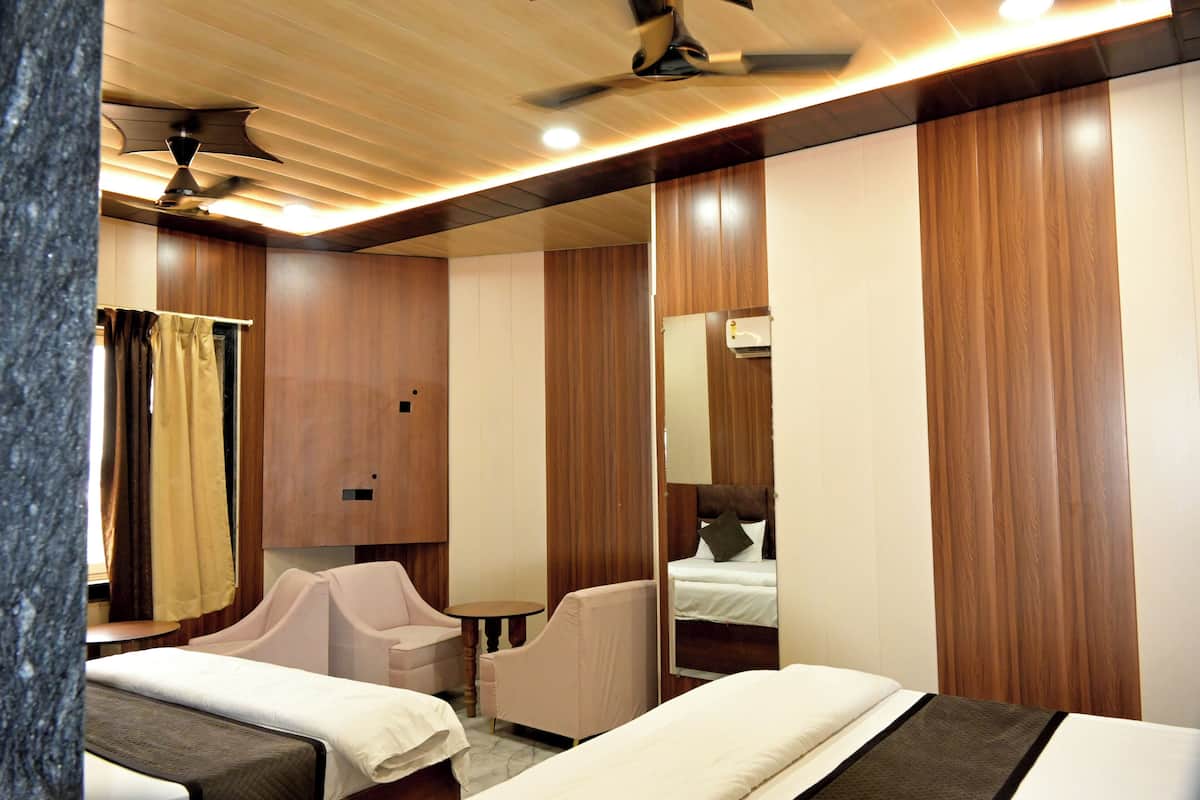 A hotel room with two beds, a sitting area with a chair and table, a ceiling fan, and wooden paneling.