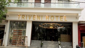 Exterior del Hotel Triveni, con una entrada destacada, escalones que conducen a la puerta y una motocicleta estacionada afuera.