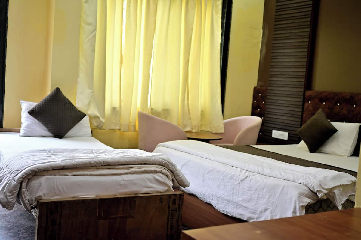 A hotel room with two beds, a wooden bench, a chair, and a window with curtains.