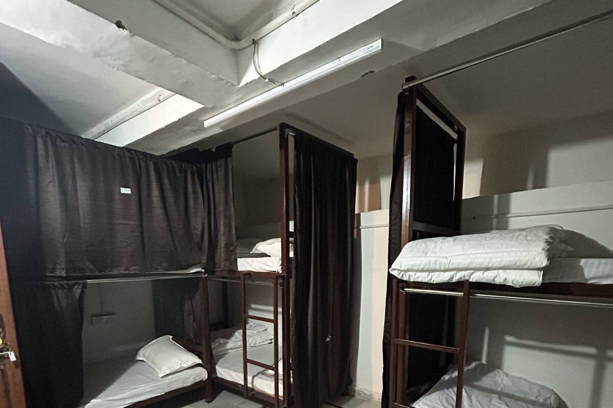Een slaapzaal met stapelbedden, een plafondventilator en een deur met gordijn.