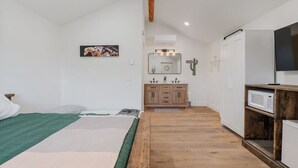 Une chambre avec un lit, un plancher en bois, une kitchenette équipée d’un four à micro-ondes et un téléviseur.