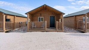 Une rangée de cabanes en rondins, dotées d’une véranda et d’une porte, construites sur un sol sablonneux.