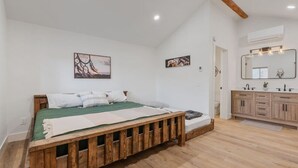 Une chambre à coucher avec un lit en bois, une couvre-lit verte et deux œuvres d’art accrochées au mur.