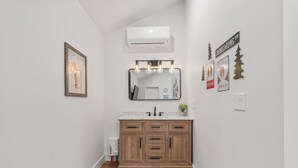 Un baño con tocador de madera, un espejo grande y aire acondicionado instalado en la pared.