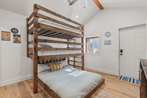 Un lit superposé avec une structure en bois, un lit recouvert d’une couverture grise, une horloge au mur et une porte avec une pancarte.
