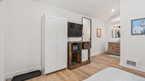 Un dormitorio con cama, armario, televisión, refrigerador pequeño y un mueble de madera.