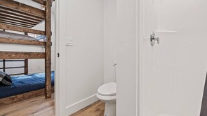 Ein Zimmer mit einem Etagenbett, einer weißen Toilette und einem Duschbereich.