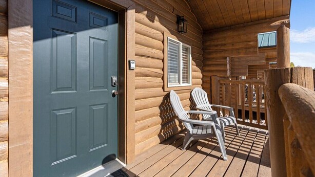 Eine Blockhütte mit einer dunkelblauen Tür, einer kleinen Veranda mit zwei Adirondack-Stühlen und einem Holzzaun.