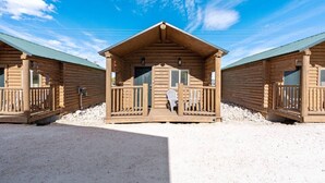 Eine Reihe von Blockhütten mit Veranda und Stuhl, gelegen auf einem Kiesplatz unter blauem Himmel.