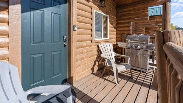 Una cabaña de madera con puerta azul, una parrilla en el exterior y una silla blanca en el porche.