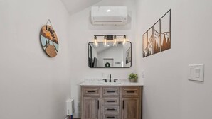 Un baño con tocador de madera, un espejo con iluminación y aire acondicionado, además de una obra de arte colgada en la pared.