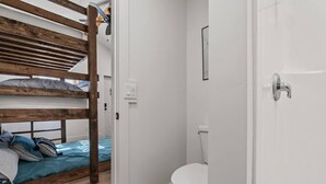 Una habitación con una cama litera, un inodoro blanco y una puerta con picaporte plateado.