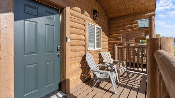 A log cabin with a wooden deck, two Adirondack chairs, and a door with a window.