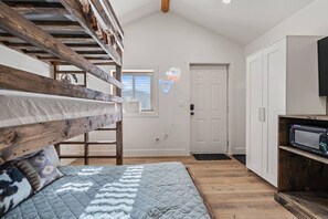 A bedroom with a bunk bed, a bedside table, a neon cow head sign, a white door, and a TV on a wooden shelf.