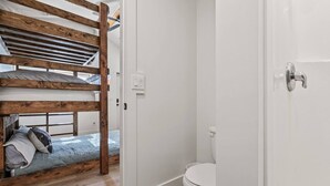 A room with a bunk bed, a white toilet, and a door leading to another room.