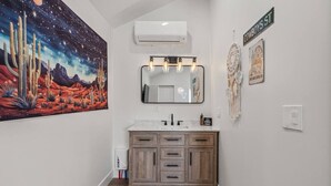 A bathroom with a large painting of a desert landscape, a wooden vanity with a mirror, and a sign that reads "COWBOYS ST".