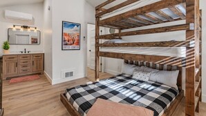 Un dormitorio con una cama nido de madera, colcha a cuadros, una mesita de noche, un espejo y un cartel en la pared.
