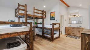 Une chambre avec des lits superposés, un plafond en bois, une salle de bain avec un lavabo et un miroir, et une affiche accrochée au mur.