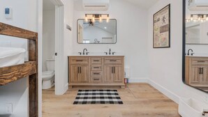 Une salle de bain avec un meuble-lavabo en bois, un tapis à carreaux noirs et blancs et un grand miroir.