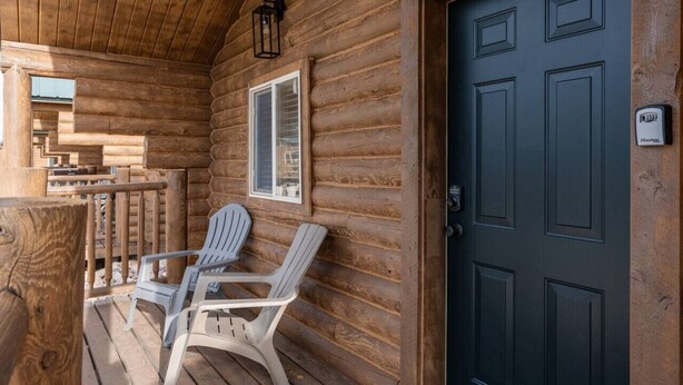 A log cabin with a wooden porch, two Adirondack chairs, a dark wooden door, and a window with shutters. - #9 Yellowstone Cabin w/ AC, Fire Pit & BBQ! (Saint Charles)