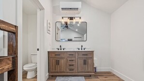 Une salle de bain avec un meuble-lavabo en bois, des toilettes blanches et un ventilateur de plafond.