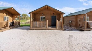 Une rangée de chalets en rondins de bois, dotés de terrasses en bois et bordés par une allée de gravier.