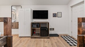 Un espace de vie compact comprenant un coin cuisine, un téléviseur à écran plat fixé au mur et un petit meuble en bois.