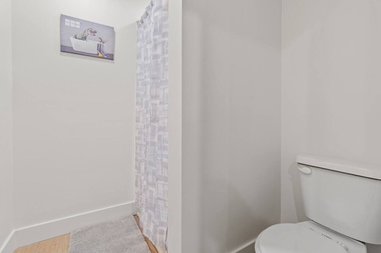 Une salle de bain avec des toilettes, un rideau de douche et une petite affiche accrochée au mur.