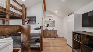 Une chambre avec un lit superposé, une armoire en bois, une télévision et une salle de bain avec un lavabo et un miroir.